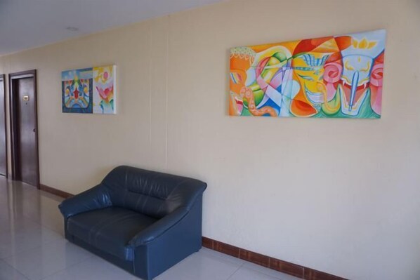 A hallway with a blue leather sofa, two colorful abstract paintings on the wall, and a door on the left. - King Hotel (Loei)