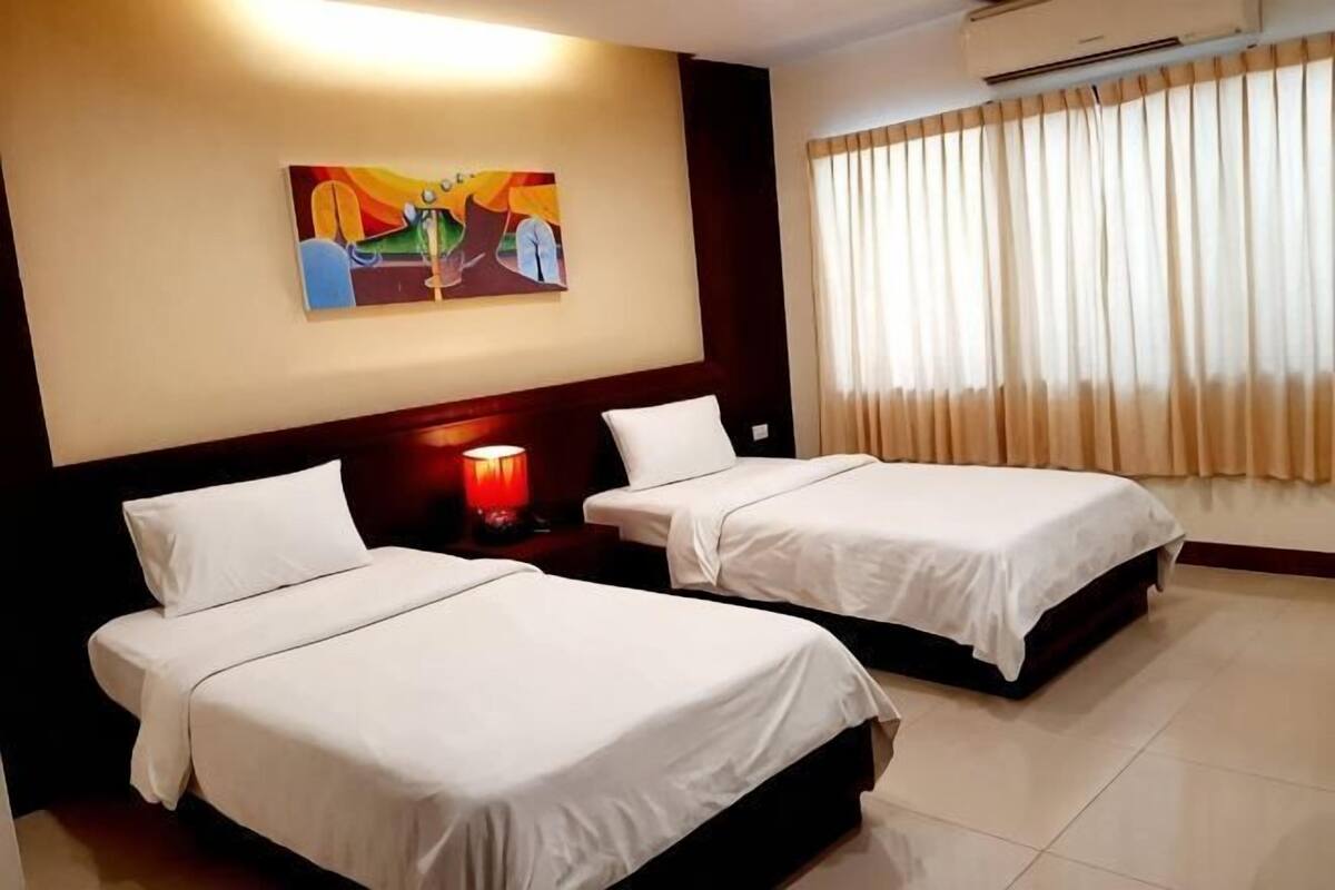 Une chambre d’hôtel avec deux lits, un tableau au mur, une table de chevet avec une lampe et une fenêtre avec des rideaux.