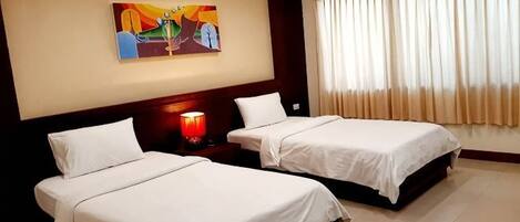 A hotel room with two beds, a painting on the wall, a nightstand with a lamp, and a window with curtains.