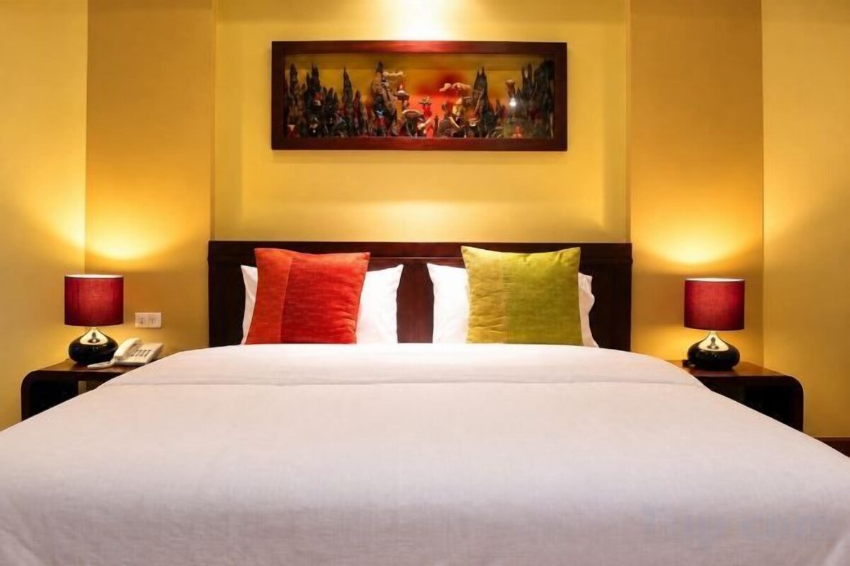 A hotel room with a large bed, two bedside lamps, and a painting on the wall.