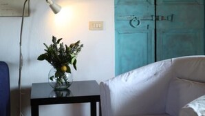 A room with a white armchair, a table with a lamp, a blue door, and a framed picture on the wall. - Le Chiusure - apartment 'Solaio' (Lake Garda, Lombardy)