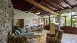 Un salon spacieux avec un plafond haut, un mur en pierre et de grandes fenêtres donnant sur un paysage verdoyant.
