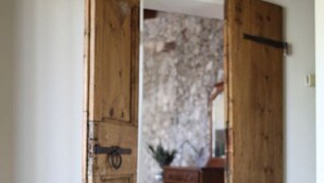 Une porte en bois ouverte donne sur une pièce dont un mur est en pierre et qui contient une commode en bois.
