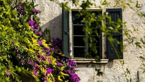 A building with a window and a door, surrounded by greenery and purple flowers. - Le Chiusure - apartment 'Fienile' (Lake Garda, Lombardy)