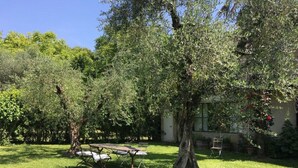 A backyard with a picnic table and chairs, surrounded by trees and a building. - Le Chiusure - apartment 'Fienile' (Lake Garda, Lombardy)
