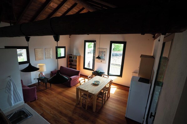 Una habitación acogedora con suelo de madera, una mesa de comedor con sillas, un sofá morado, una estantería y una ventana con vistas a zonas verdes.