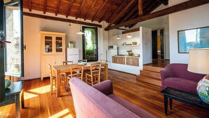 A spacious living area with a wooden dining table and chairs, a purple sofa, and a kitchen area with cabinets and a refrigerator. - Le Chiusure - apartment 'Fienile' (Lake Garda, Lombardy)