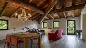 A spacious loft with exposed wooden beams, a wooden dining table with chairs, a red armchair, and a chandelier. - Le Chiusure - home 'Castello' (Lake Garda, Lombardy)