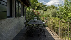 A wooden deck with a table and chairs, surrounded by a metal fence and lush greenery. - Le Chiusure - home 'Castello' (Lake Garda, Lombardy)