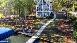 A two-story house with a covered porch and a small deck, surrounded by a wooded area and a clear path leading to a dock over water. - Cozy Cottage at Lake Oconee • Walk-Out Patio • Scenic Porch • Sleeps 8 (Eatonton)