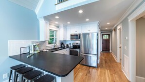 A modern kitchen with white cabinets, stainless steel appliances, and a central island with bar stools. - Cozy Cottage at Lake Oconee • Walk-Out Patio • Scenic Porch • Sleeps 8 (Eatonton)