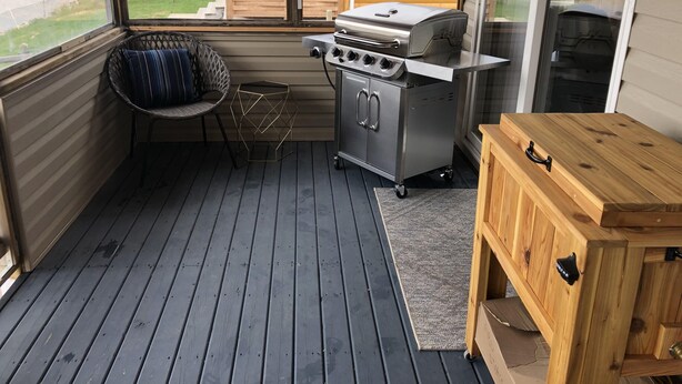 Een klein, afgesloten buitenruimte met een barbecue, een stoel en een houten tafel.