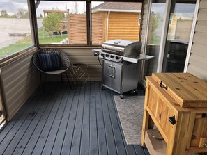 A small, enclosed outdoor space with a grill, a chair, and a wooden table. - Water Front Cottage near Waterton (30 min) (Hill Spring)