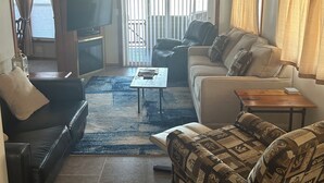 Een woonkamer met een zwarte leren bank, een fauteuil met een patroon, een houten salontafel en een televisie op een kast.