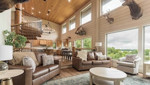 A spacious living area with leather sofas, a wooden coffee table, and a staircase with a chandelier.