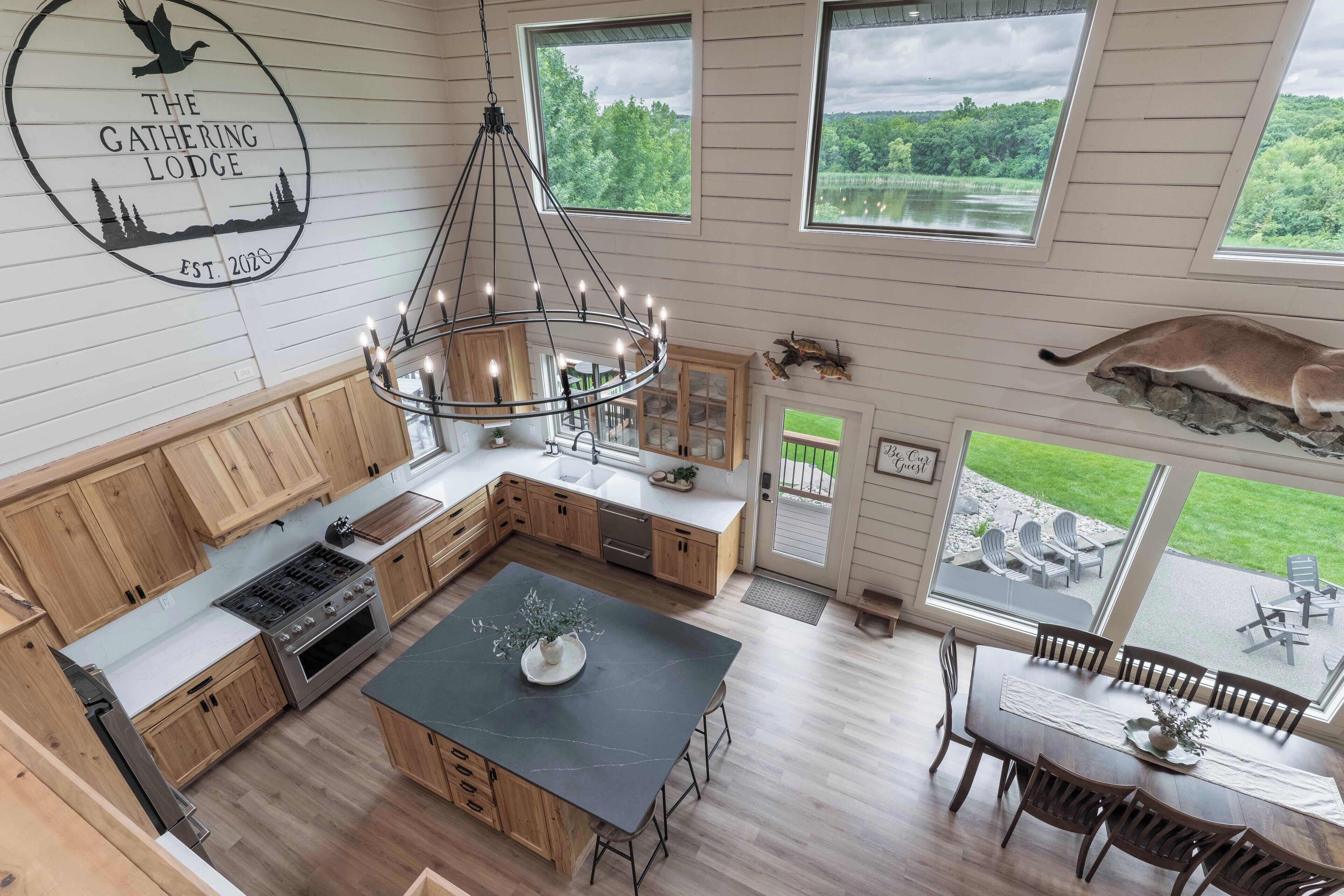 Une cuisine moderne avec des meubles en bois, un îlot central et un coin repas offrant une vue sur l’extérieur.