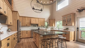 A modern kitchen with wooden cabinets, a central island with stools, and a logo on the ceiling.