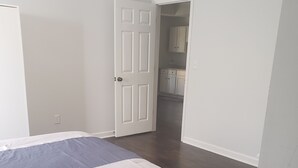 Un dormitorio con una cama, una puerta que da a una cocina y una pared blanca.