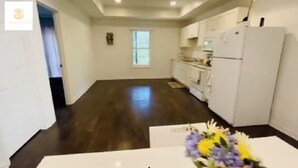Una cocina amplia con pisos de madera oscura, armarios blancos y un refrigerador.