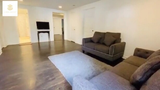 Un salón amplio con un sofá gris, una mesita auxiliar y un televisor de pantalla plana.