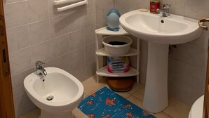 A bathroom with a bidet, a sink, and a mirror. There are toiletries on the sink and a blue mat on the floor. - Casa Marina (Sardegna)