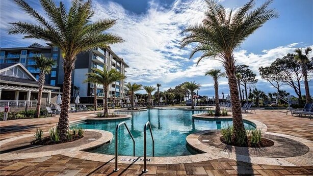 A swimming pool surrounded by palm trees and lounge chairs, with a hotel building in the background. - Spectacular Oceanview, Oceanfront Heated Pool! (Hilton Head Island)