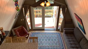 Una stanza accogliente con soffitto spiovente, una ventola a soffitto, un tappeto decorato, un divano e vista su un patio in legno.