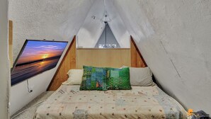 Una stanza accogliente a forma di triangolo con un letto, un'ampia finestra che mostra un tramonto e una testiera in legno.