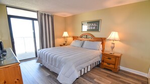 A hotel room with a large bed, two bedside tables with lamps, a wooden dresser, and a sliding glass door to the balcony. - 20% off weekly stays thru Sept. Sat to Sat. 4BR OF condo. Ocean Drive.  Sleeps 12. (North Myrtle Beach)