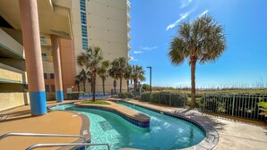 A swimming pool with a curved design, surrounded by palm trees and a fence. - 20% off weekly stays thru Sept. Sat to Sat. 4BR OF condo. Ocean Drive.  Sleeps 12. (North Myrtle Beach)