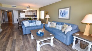 A living room with a blue sectional sofa, a wooden coffee table, and a lamp. - 20% off weekly stays thru Sept. Sat to Sat. 4BR OF condo. Ocean Drive.  Sleeps 12. (North Myrtle Beach)