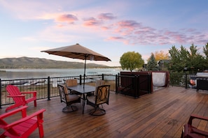 A wooden deck with outdoor furniture, a grill, and a view of a lake and mountains. - 3 Cubs Lakefront Cabin - Lakefront, Dock, Hot Tub, Foosball, Ping Pong, Lake View (Big Bear Lake)