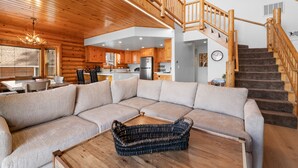 A spacious living area with a large sectional sofa, a wooden coffee table, and a staircase leading to an upper level. - 3 Cubs Lakefront Cabin - Lakefront Big Bear Cabin w/ Hot Tub & Game Table (Big Bear Lake)