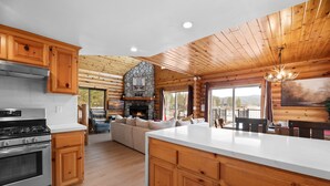 A log cabin interior with a kitchen, dining area, and a stone fireplace. - 3 Cubs Lakefront Cabin - Lakefront Big Bear Cabin w/ Hot Tub & Game Table (Big Bear Lake)