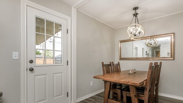 Un coin repas avec une table et des chaises en bois, une porte blanche avec une fenêtre et un lustre.