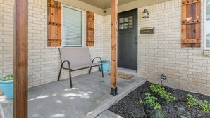 Une véranda avec un banc, une porte et un mur en briques agrémenté de volets en bois.