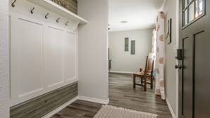 Un couloir avec un mur blanc, un mur d’accent en bois, un panneau d’accueil, un porte-manteau, une chaise et une porte.