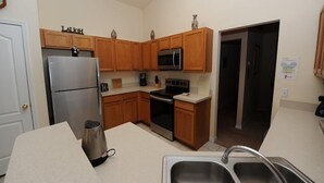 A compact kitchen with wooden cabinets, a stainless steel refrigerator, a microwave, an oven, and a sink. - Sandy Ridge 76 (Davenport)