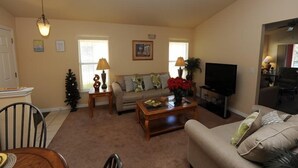 A living room with a sofa, coffee table, TV, and a dining area with chairs and a table. - Sandy Ridge 76 (Davenport)