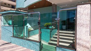 A hotel entrance with glass doors, a tiled wall, and a staircase leading inside. - Zancanaro 102- Apto - 641B (Bombinhas)