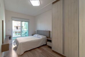 Une chambre à coucher comprenant un lit, des tables de chevet, une armoire et une porte-fenêtre coulissante donnant sur un balcon.