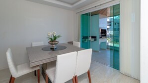 A dining area with a table and chairs, a vase with flowers, and a view through a glass door to an outdoor space. - Zancanaro 102- Apto - 641B (Bombinhas)