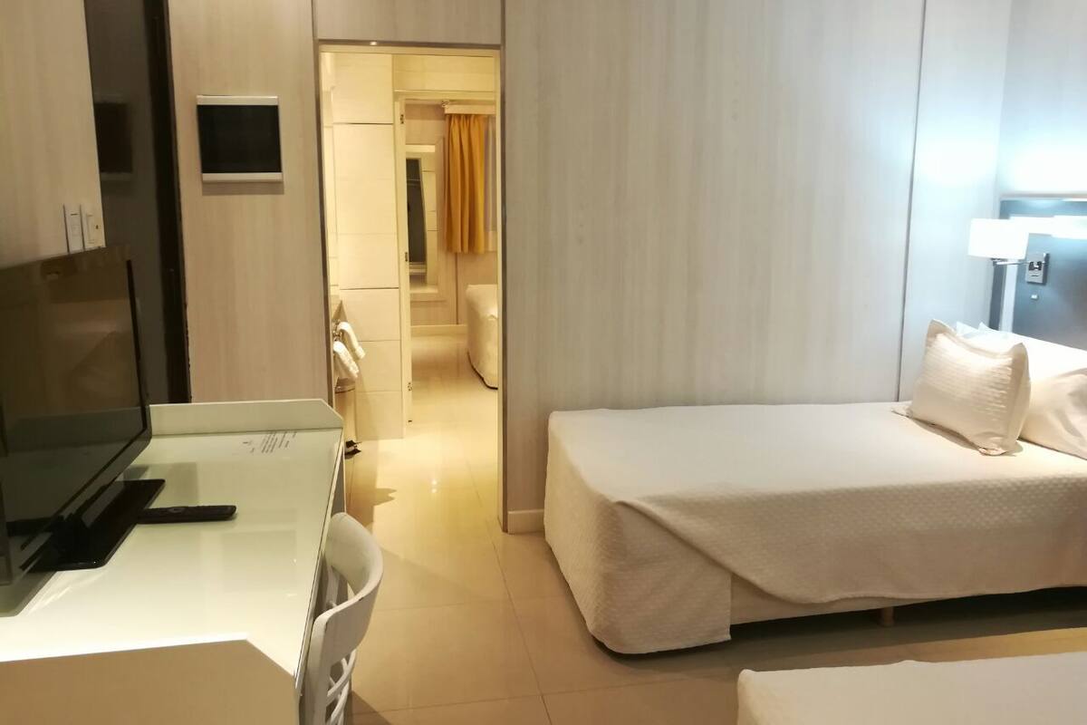 Ein Hotelzimmer mit einem Bett, einem Schreibtisch mit Fernseher und einem durchgehenden Tür sichtbar erkennbaren Badezimmer.