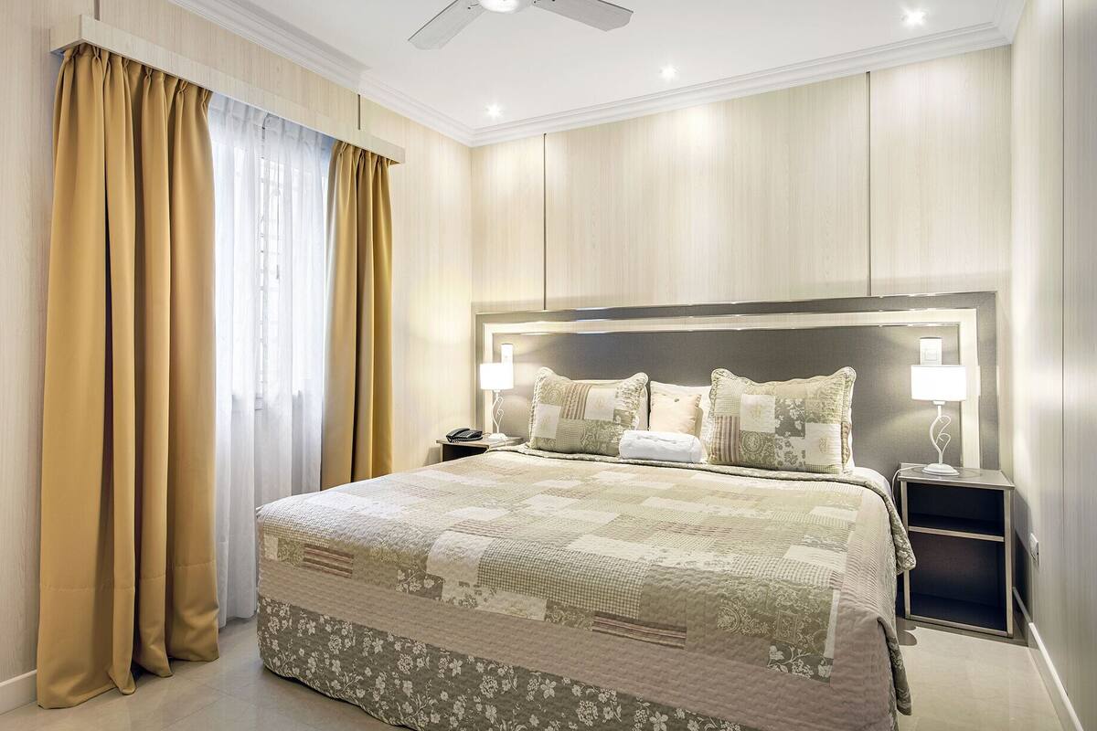 Ein Hotelzimmer mit einem großen Bett, einem Nachttisch, einem Deckenventilator und einem Fenster mit Vorhängen.