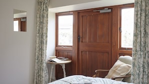 Une chambre à coucher avec un lit, une chaise, une petite table et une fenêtre avec des rideaux.