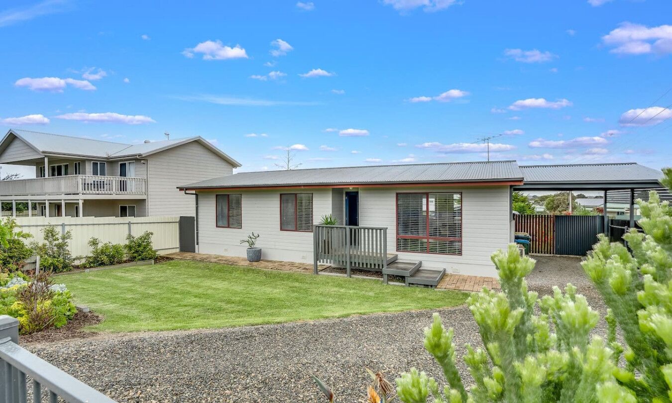 A two-story house with a covered patio, a well-maintained lawn, and a gravel driveway.