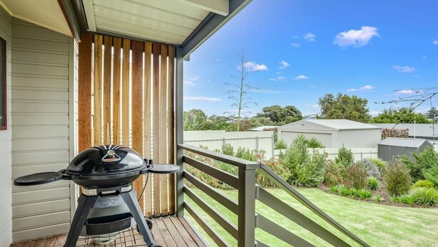 Un balcon doté d’un barbecue, de lambris en bois et offrant une vue sur un quartier résidentiel avec des maisons et de la verdure.