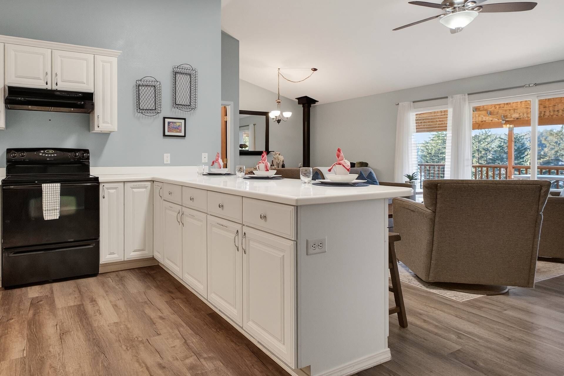 A modern kitchen with white cabinetry, a black stove, and a dining area with a brown chair.
