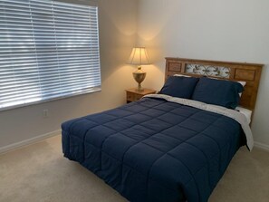 A bedroom with a bed, a nightstand with a lamp, and a window with blinds. - Terra Verde 693 (Kissimmee)
