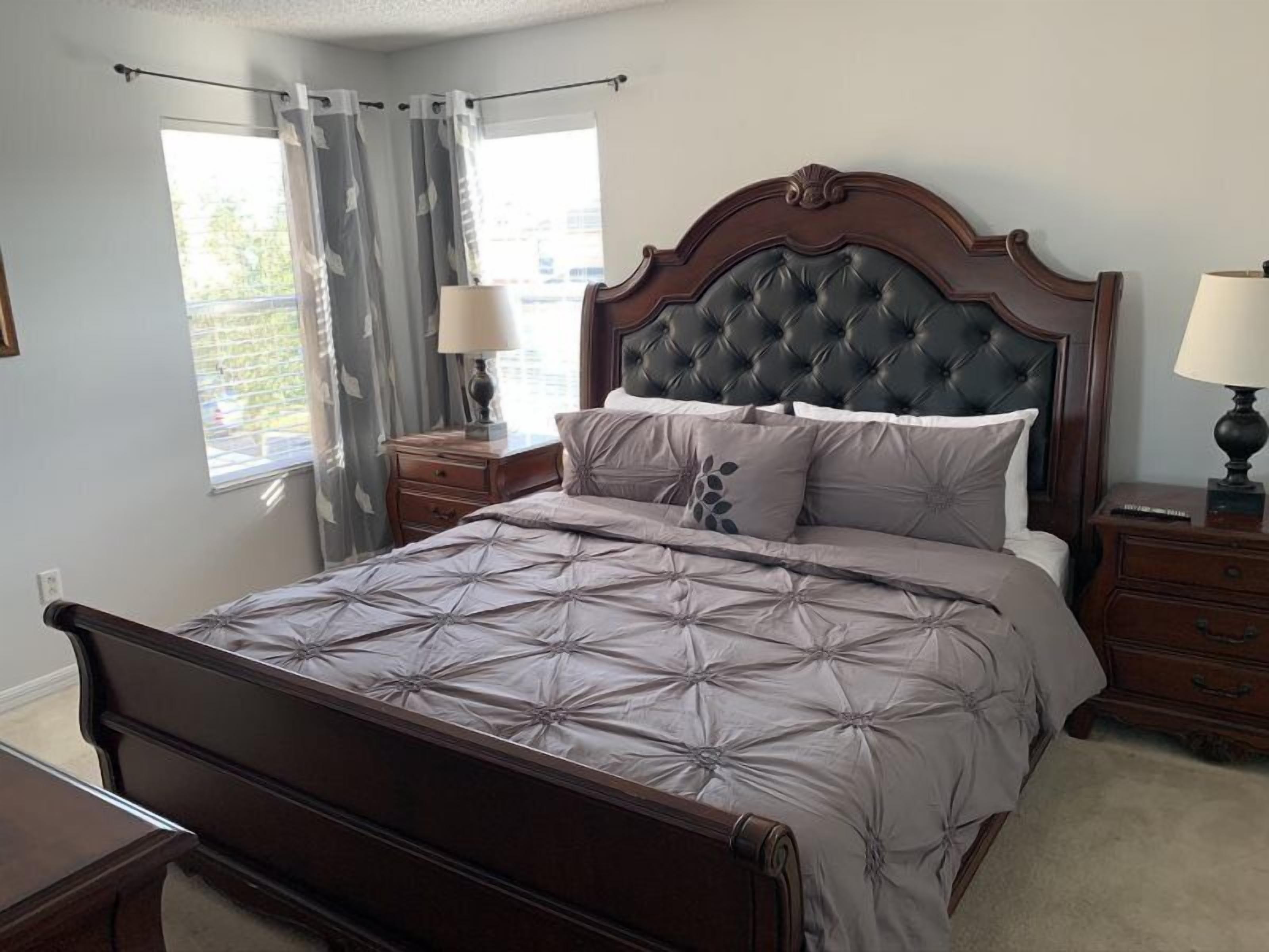 A bedroom with a large bed, two nightstands, a wooden headboard, and a window with curtains.